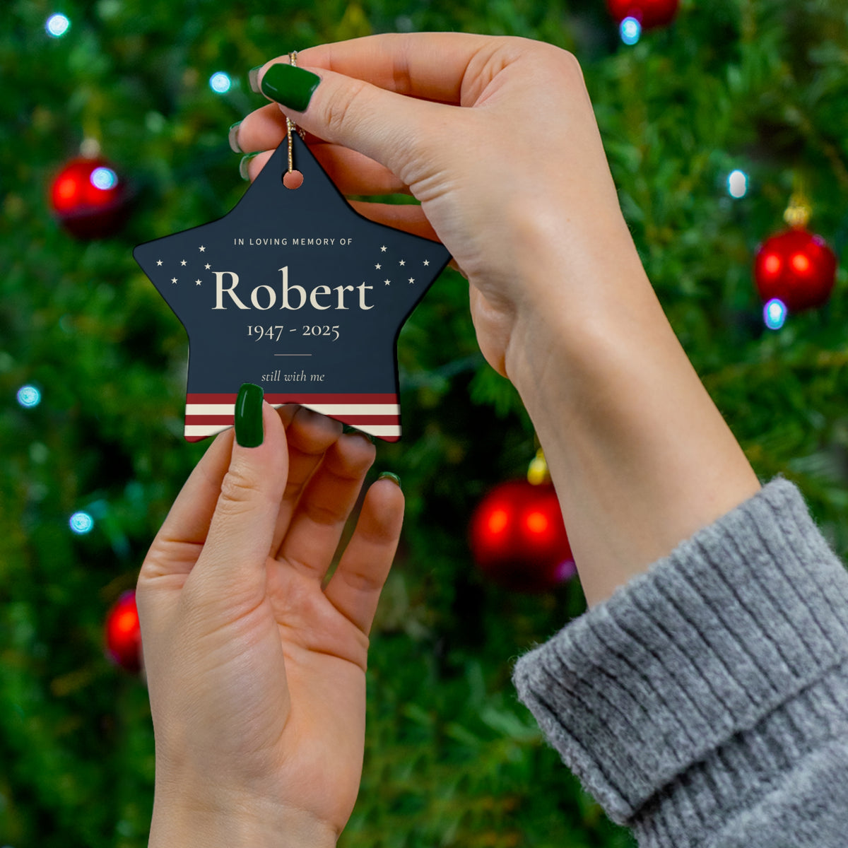 American flag star memorial ornament with the name Robert held in front of a Christmas tree