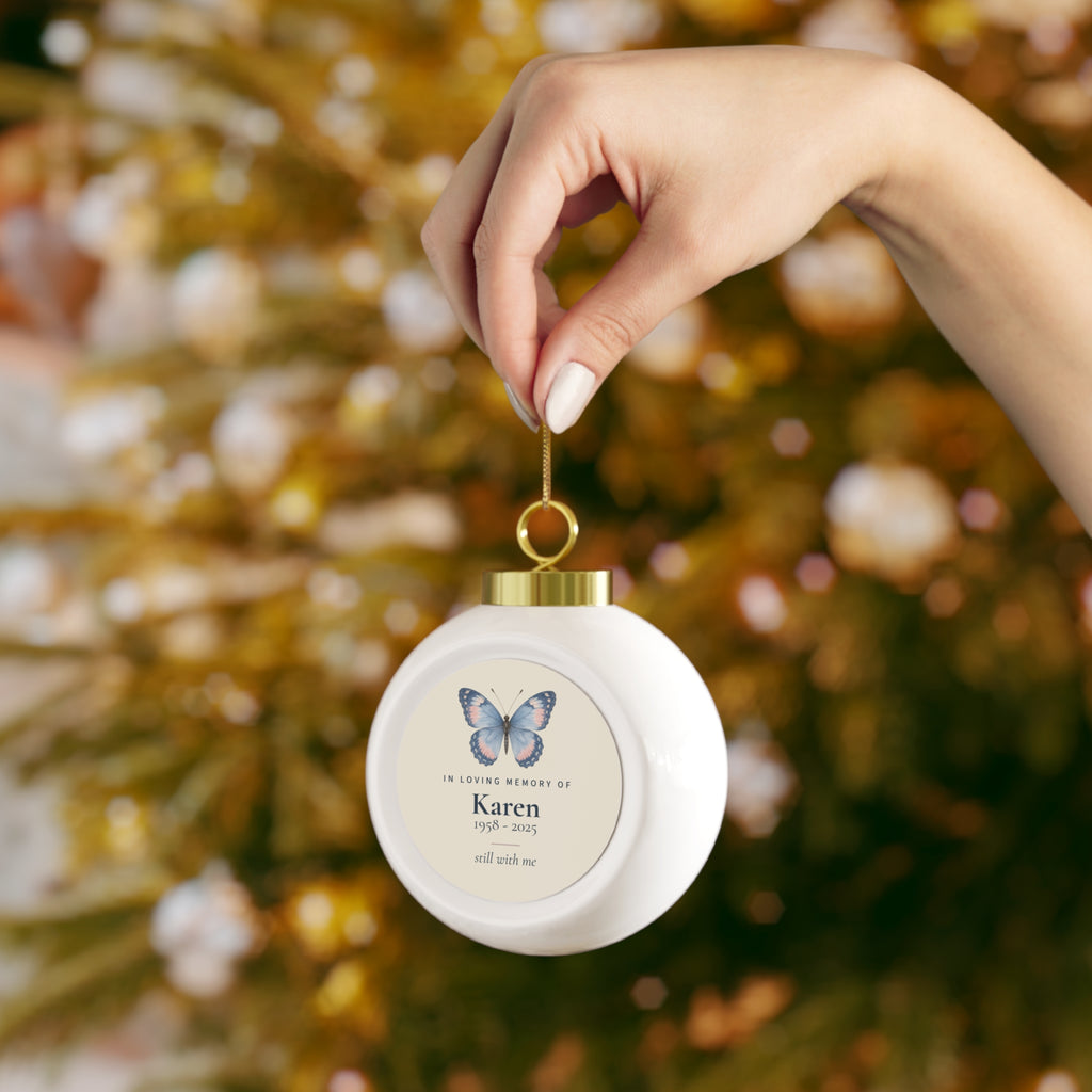Hand holding the butterfly memorial Christmas ball by its gold ribbon
