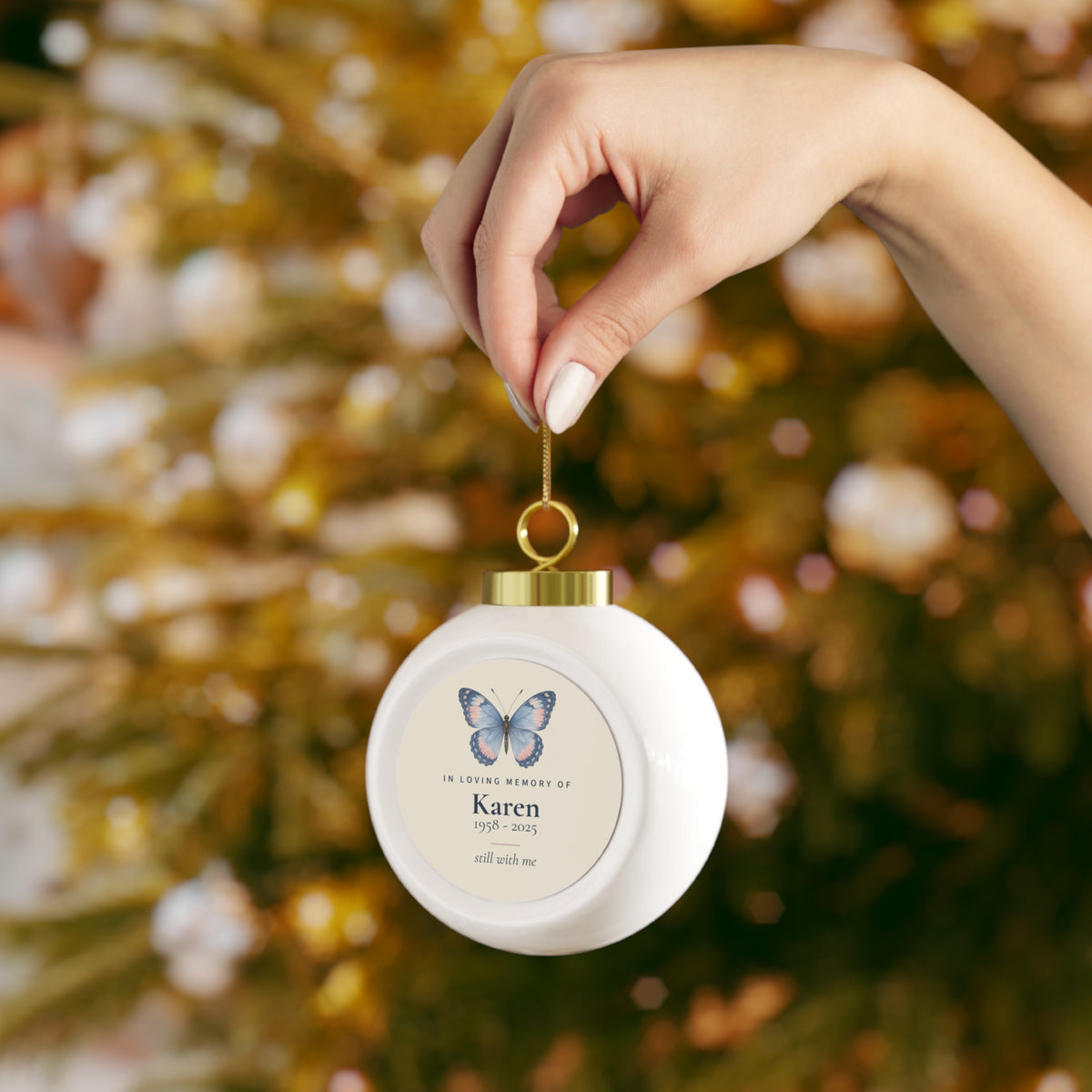Butterfly memorial Christmas ball held up in front of Christmas lights