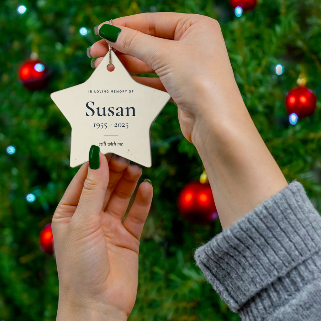 Cream star memorial ornament with the name Susan held in front of a Christmas tree