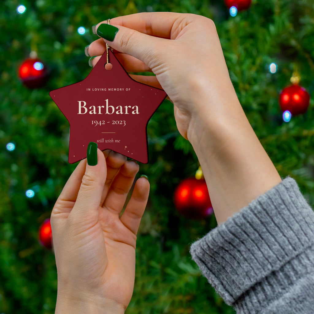 Red star memorial ornament with the name Barbara held in front of a Christmas tree