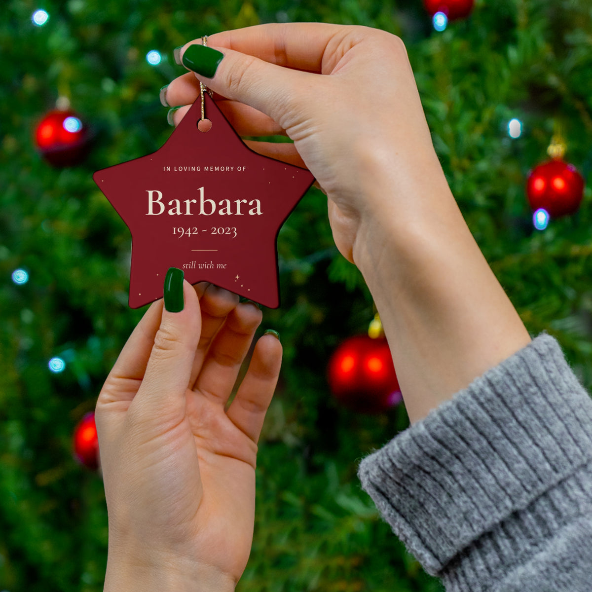 Red star memorial ornament with the name Barbara held in front of a Christmas tree