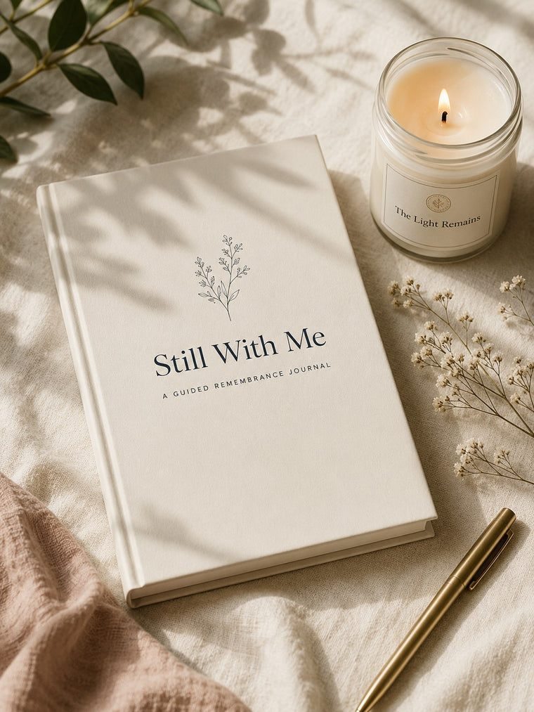 Eine brennende Sojawachskerze „The Light Remains“ neben dem Still-With-Me-Journal, dazu Schleierkraut und ein goldener Stift auf warmem Leinen